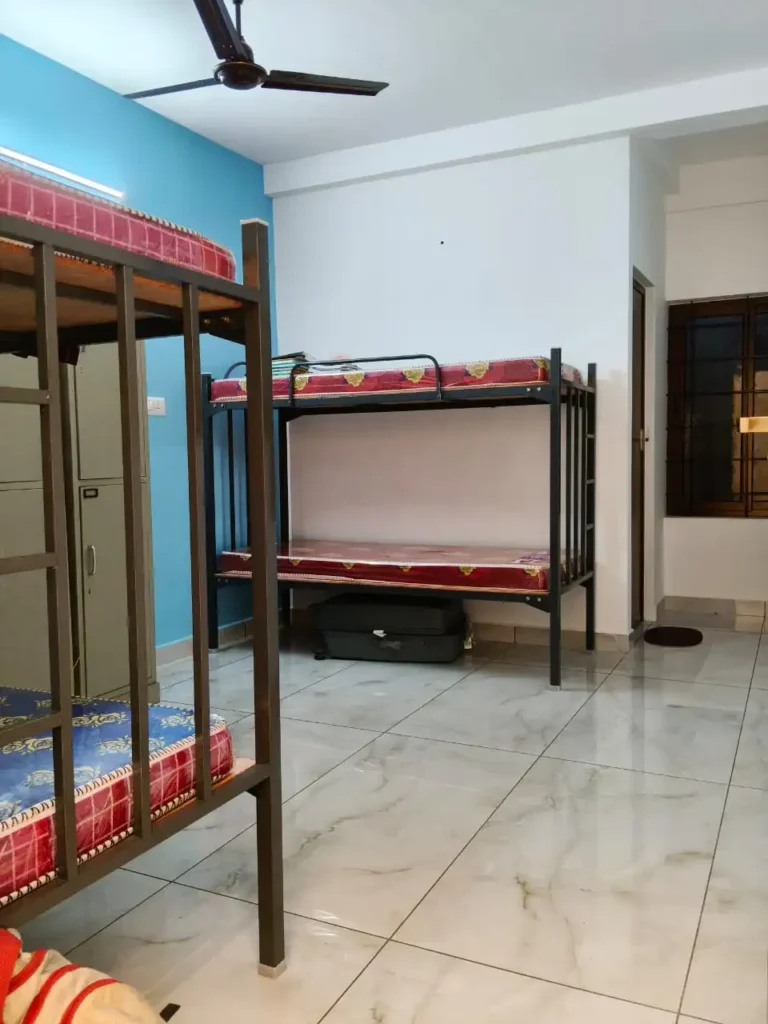 A brightly lit, spacious resident room at Amelia Ladies Hostel in Kakkanad, featuring neatly made beds, premium wardrobes, and a clean, organized layout.