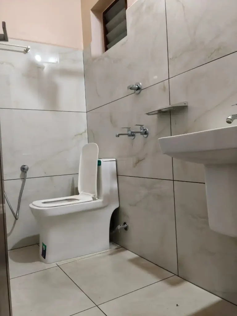 A clean, modern, and well-tiled attached bathroom featuring high-quality sanitary fittings and a professional finish at a ladies' hostel in Kakkanad, Kochi.